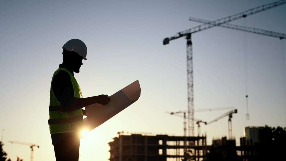 Builder, engineer or architect in helmet checking drawings at construction site.